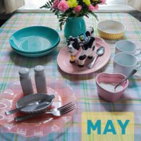 Ladies tea table with mugs sugar cow shaped creamer aqua salad bowls on a pastel plaid tablecloth