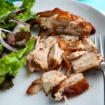 marinated chicken thighs on a white dinner plate with salad served and a platter of chicken in background