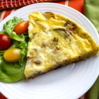 one slice of potato and onion frittata with lettuce and grape tomatoes on the side