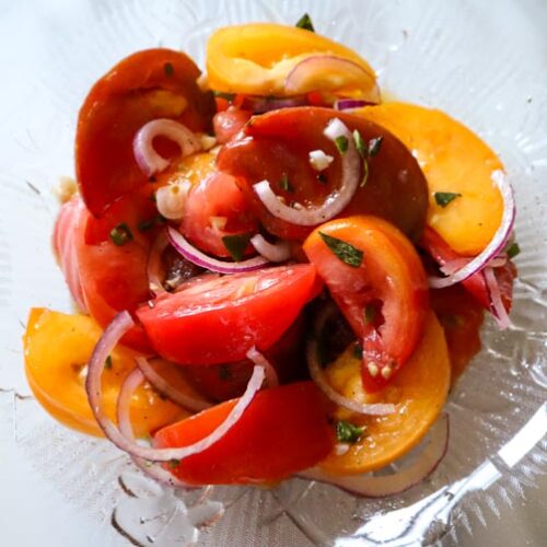 tomato salad made with heirloom tomatoes of all colors served in a glass serving bowl on a marble table
