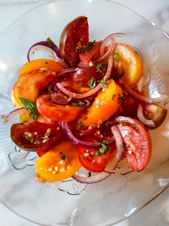 tomato salad in a glass bowl made with heirloom tomaotes red onion and basil.