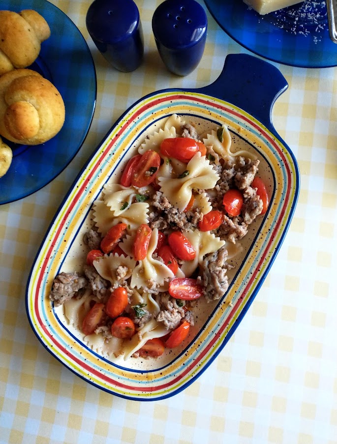 grape tomatoes and italian sausage meat over pasta served in oval dish with checkered yellow tablecloth