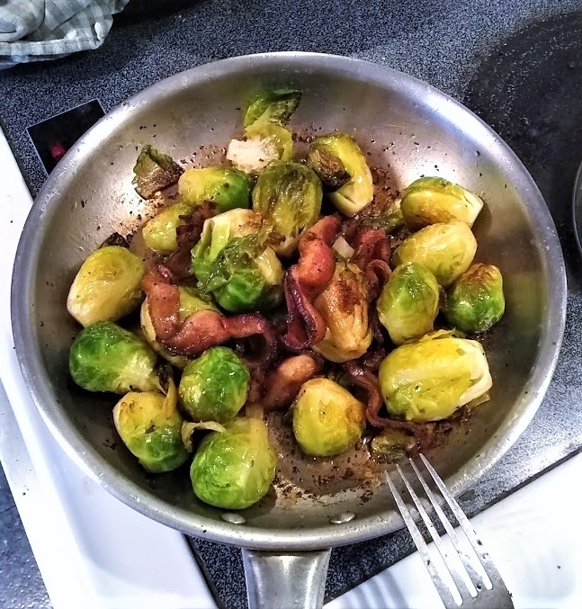 brussels sprouts in skillet are done and cooked and torn pieces of bacon are added