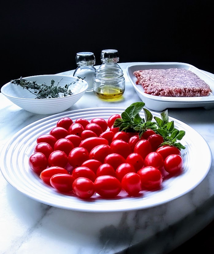 grape tomato and sausage ingredients grape tomatoes sausage meat oregano salt pepper olive oil on white table