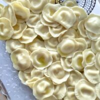 a clear serving dish full of cooked cheese ravioli