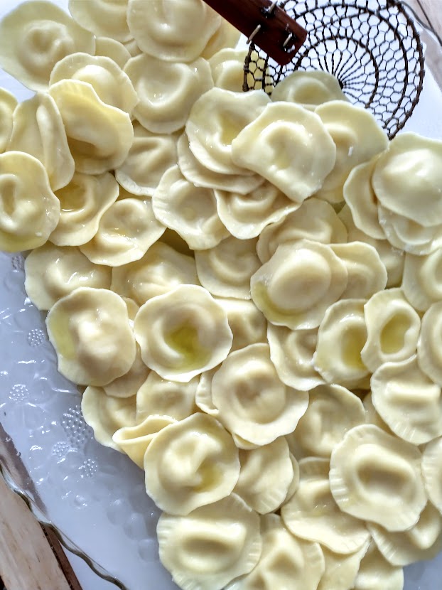 a clear serving dish full of cooked cheese ravioli