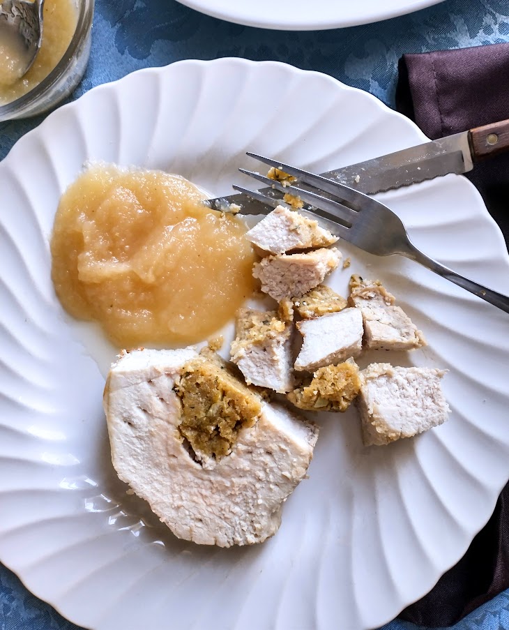 slice of stuffed pork loin roast on a white plate served with applesauce