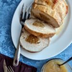 stuffed pork loin roast on a serving platter with a side dish of applesauce