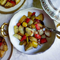 roasted summer vegetables green and yellow peppers plum tomatoes potatoes onion served in a gold and ivory serving dish