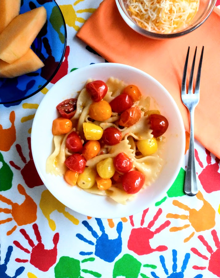 multi colored grape tomatoes with bowtie pasta served in a white bowl with shredded cheese and melon on the table