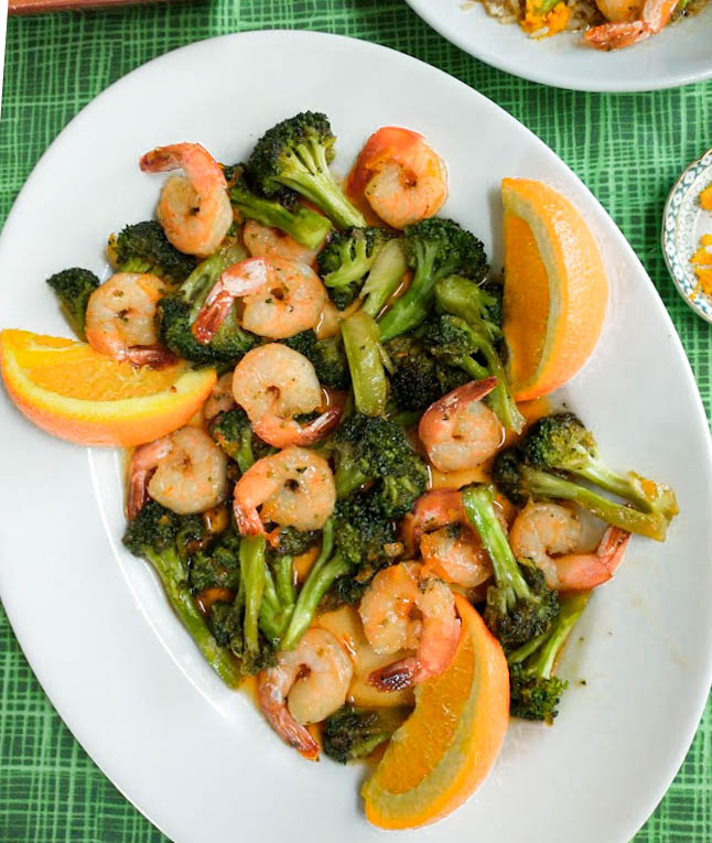 shrimp with broccoli in a homemade orange sauce served on a platter with orange wedges