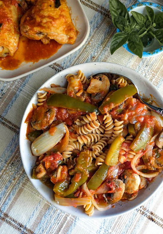 chicken cacciatore ,a serving bowl with cacciatore vegetables in sauce mixed with rotini pasta chicken in background