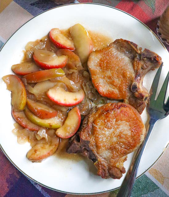 pork chops apples and onions in a sweet and savory cider sauce served on a platter