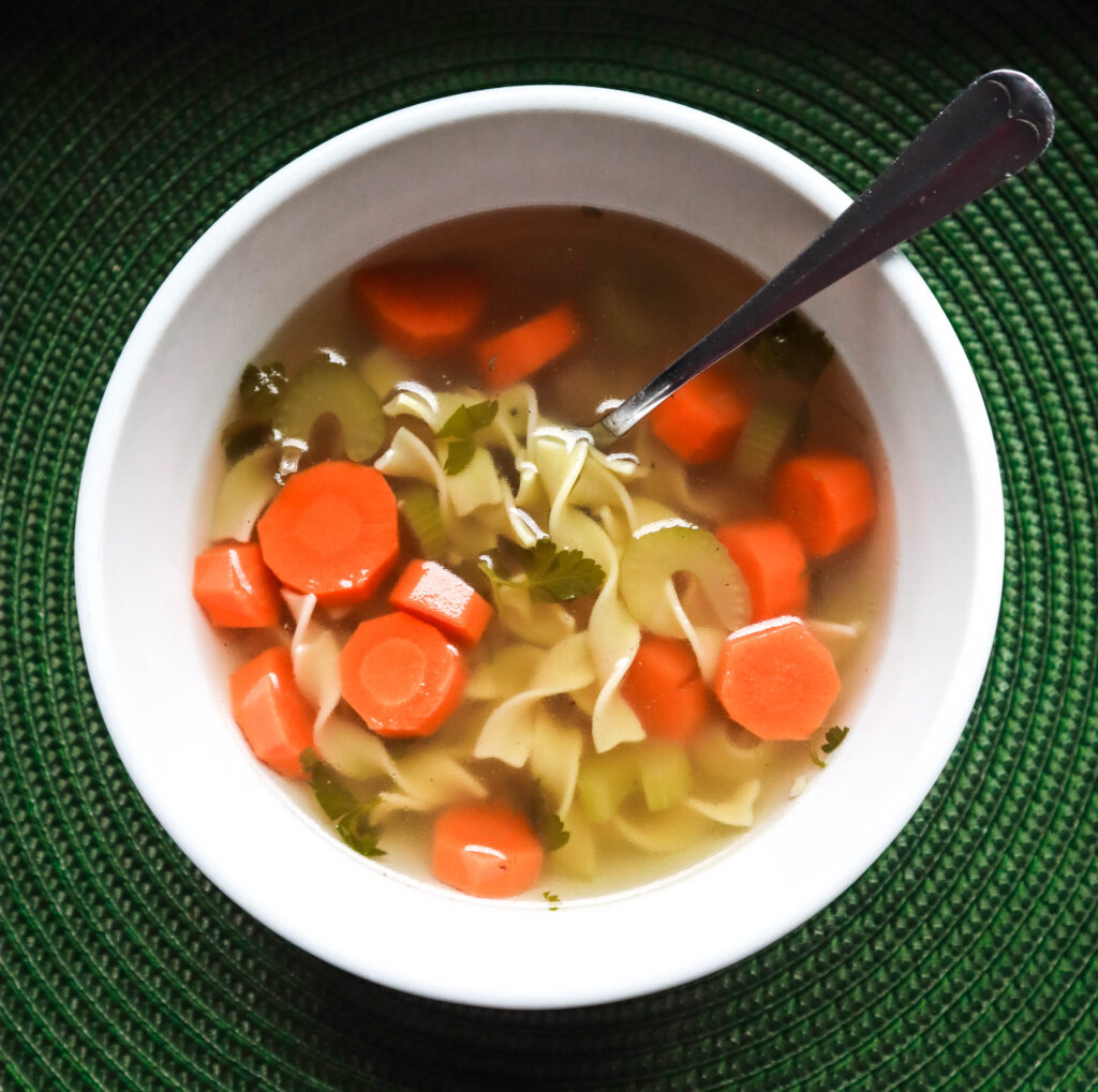 homemade vegetable noodle soup made from homemade stock served in a white bowl