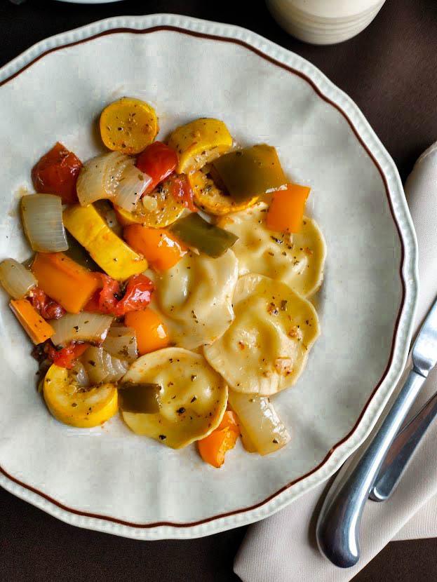 roasted vegetables orange and green peppers yellow squash onion and tomato with round cheese filled ravioli on single serve ivory plate