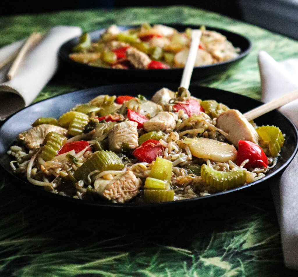 chicken stir fry served in black bowl side view with chopsticks