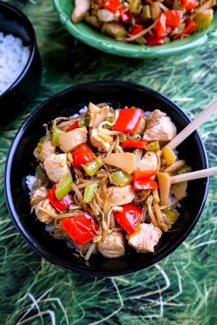 chicken stir fry served over rice in a black bowl with chop sticks