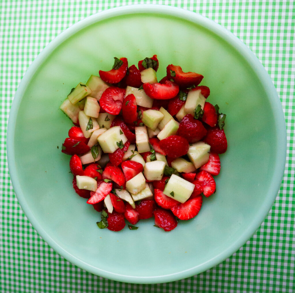 green mixing bowl with the chopped ingredients for strawberry salad, lemon juice and honey. 