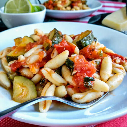 zucchini and tomato sauce with pasta served on a white plate on red and white tablecloth