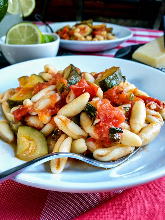 zucchini and tomato sauce with pasta served on a white plate on red and white tablecloth