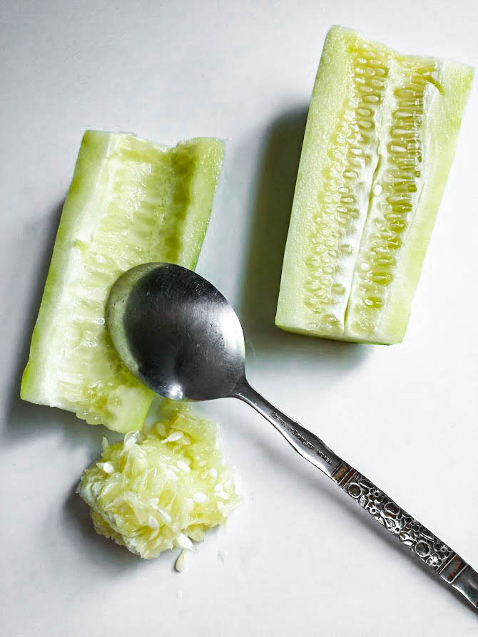 using a spoon to scrape the seeds from a cucumber