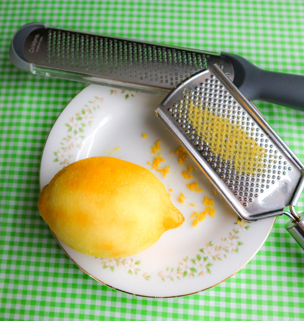 a lemon on a white plate with some zest grated off and 2 graters. 