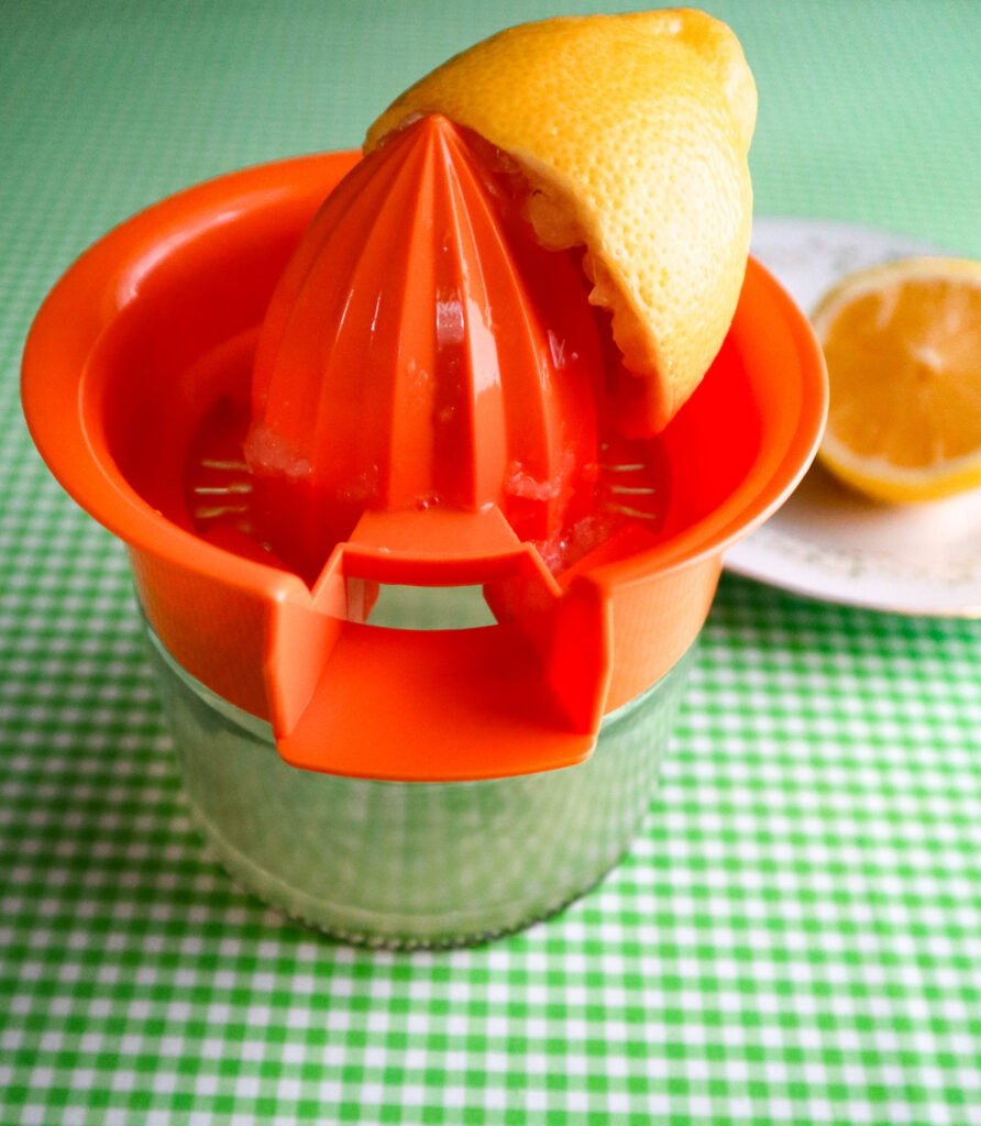 a lemon juicer with a half lemon already squeezed and the other half in the background.