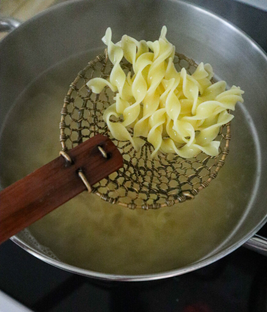 a slotted spoon with drained noodles over the saucepan with water they were cooked in