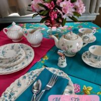 dinner table setup in teal and pink lots of flowers on dishes tablecloth and in a vase