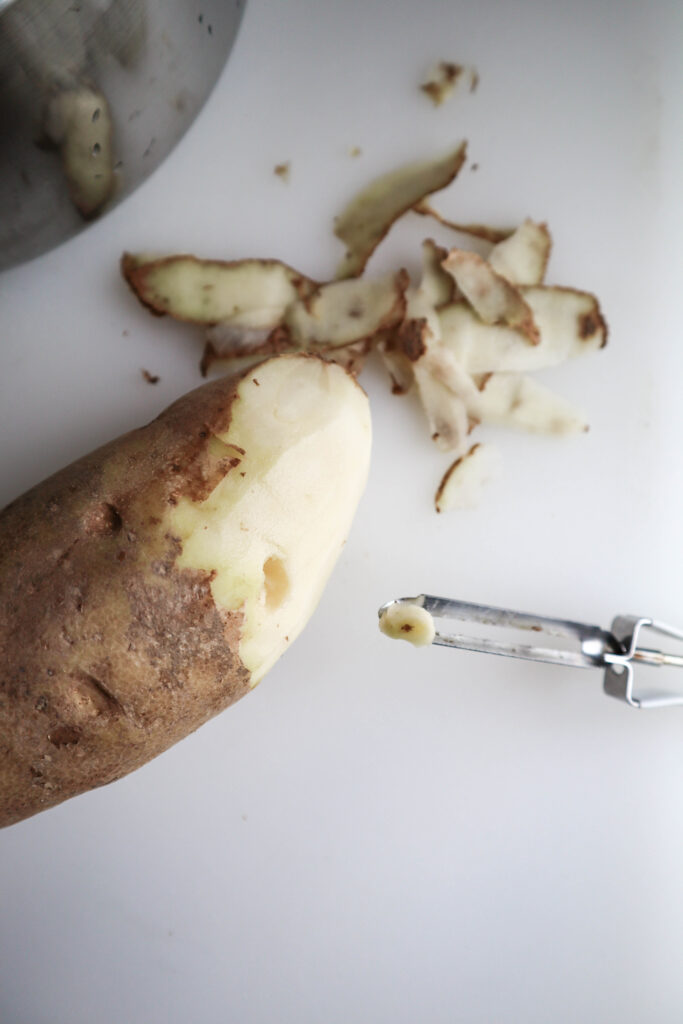 potato being peeled with a vegetable peeler