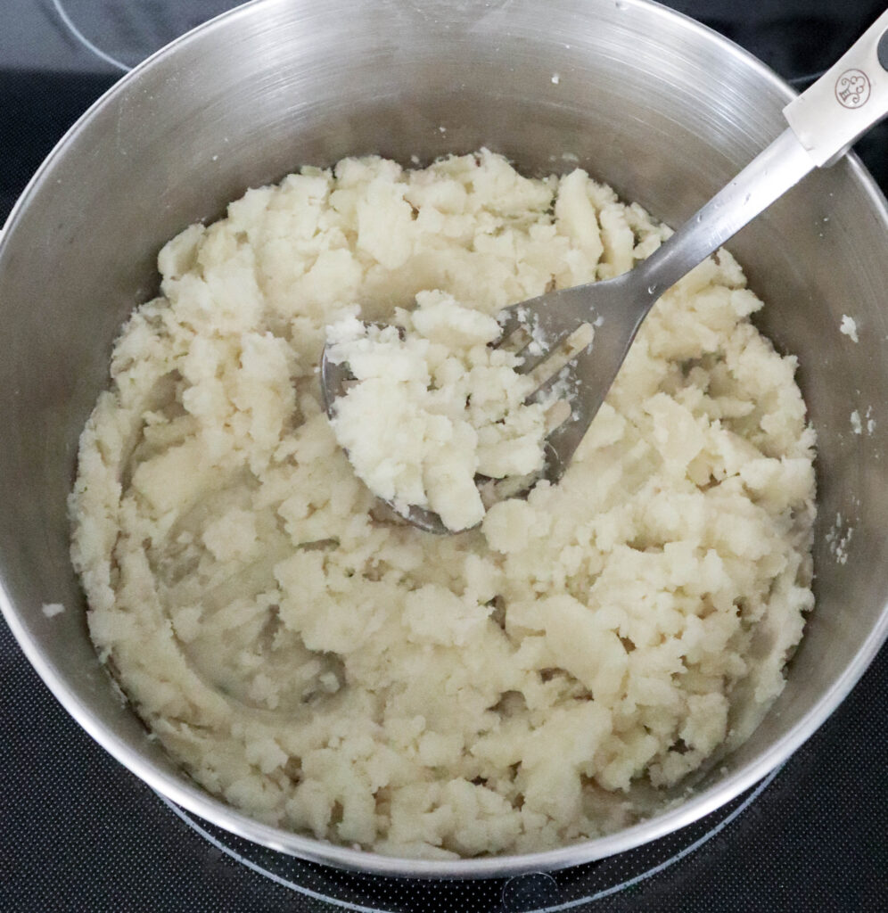 mashing potatoes in pan with masher