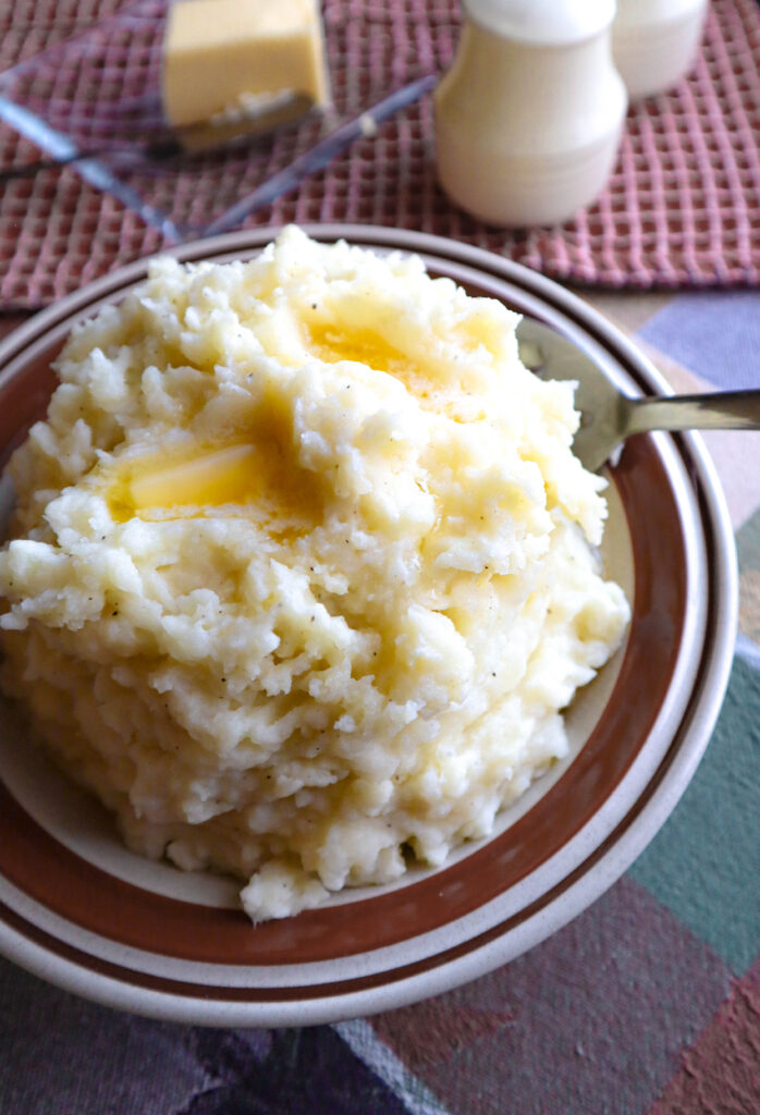 heaping bowl of mashed potatoes with butter dripping from top to bottom table and dishes in ivory and brown