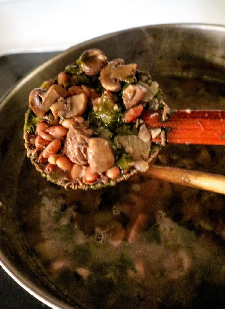 beef and beans stew done on the stove ingredients lifted out of the stew with a spider mesh spoon