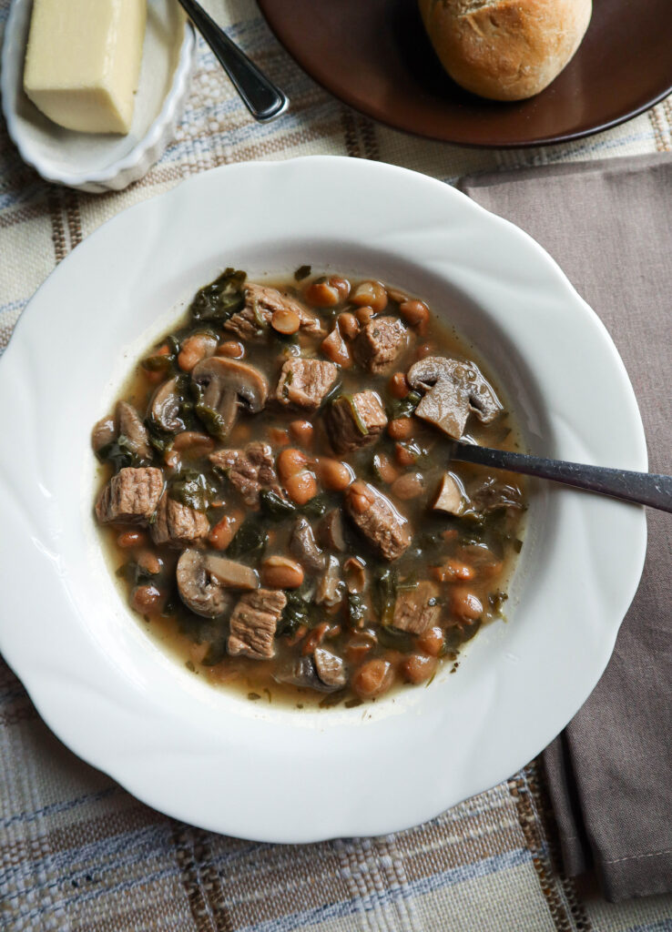 beef and beans stew with mushrooms and spinach served in a white bowl