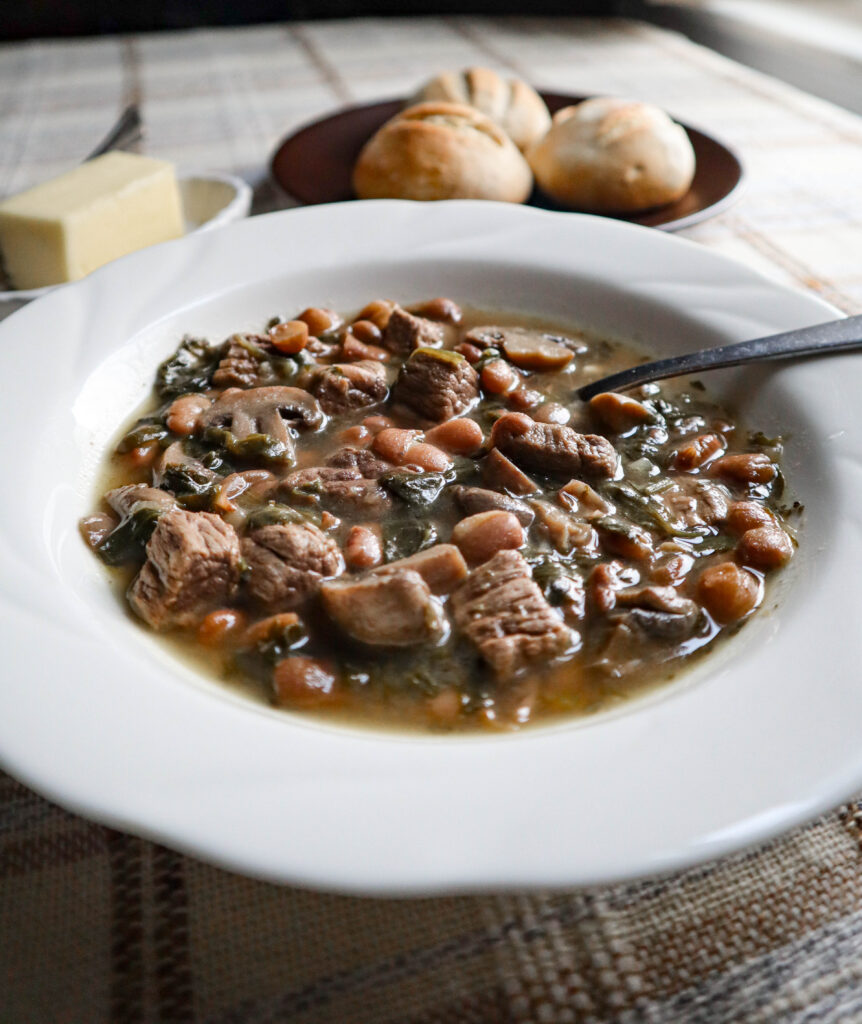 beef and beans stew with mushrooms and spinach served in a white bowl