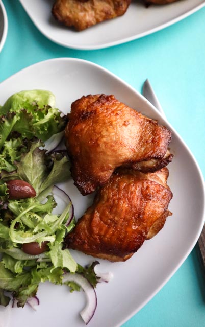 chicken thighs on a white plate with salad on the side