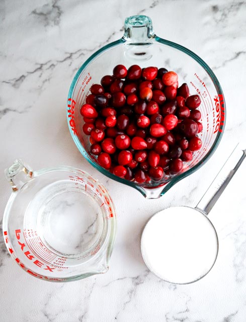 ingredients to make homemade cranberry sauce a measuring cup with fresh cranberries, a cup of white sugar and water