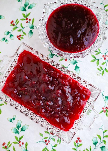 homemade whole berry and jellied cranberry sauce served in glass dishes on a white holiday tablecloth